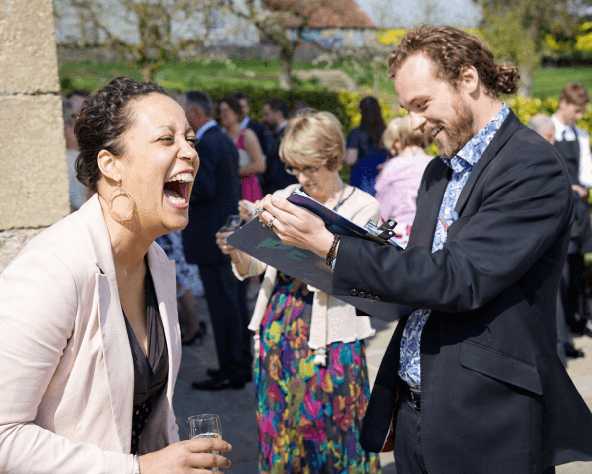 Guests laughing with a caricature artist at a wedding reception